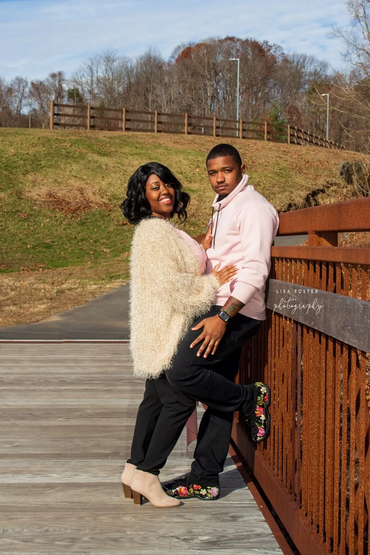 Couple leaning on a footbridge rail, smiling at the camera