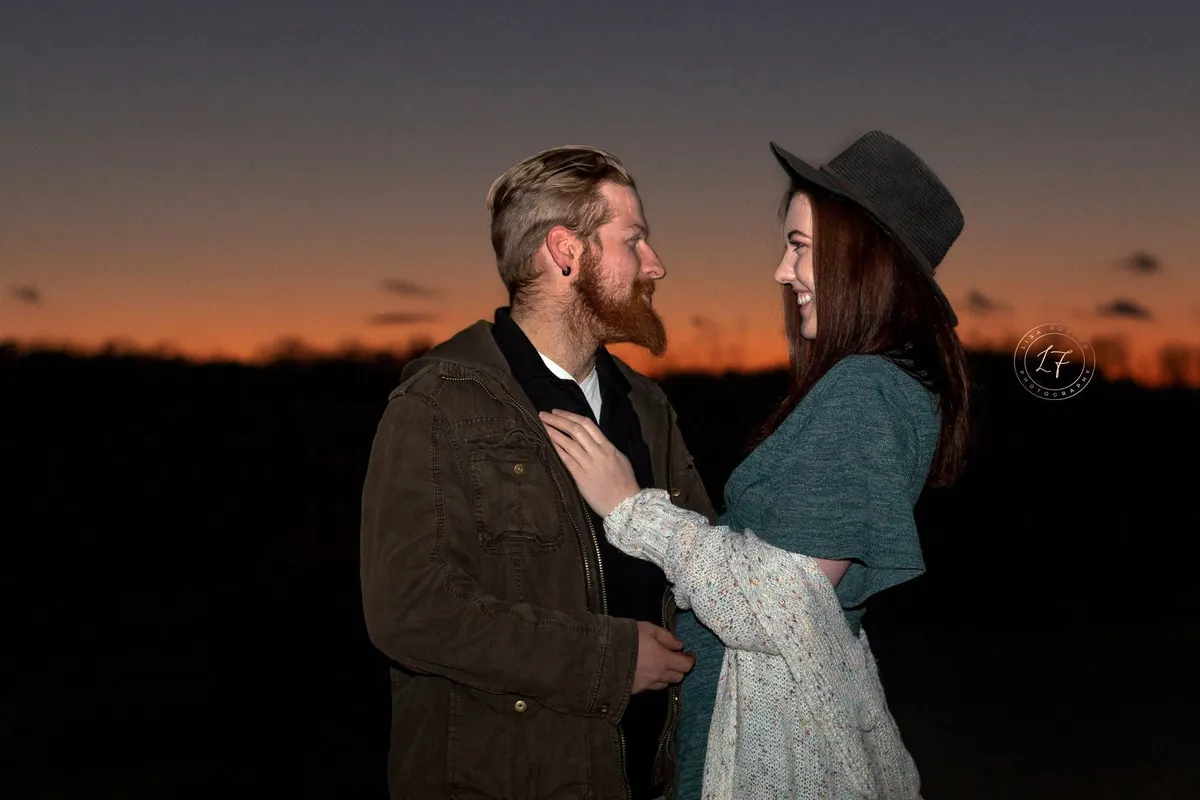 Engaged couple embracing against a glowing orange sunset