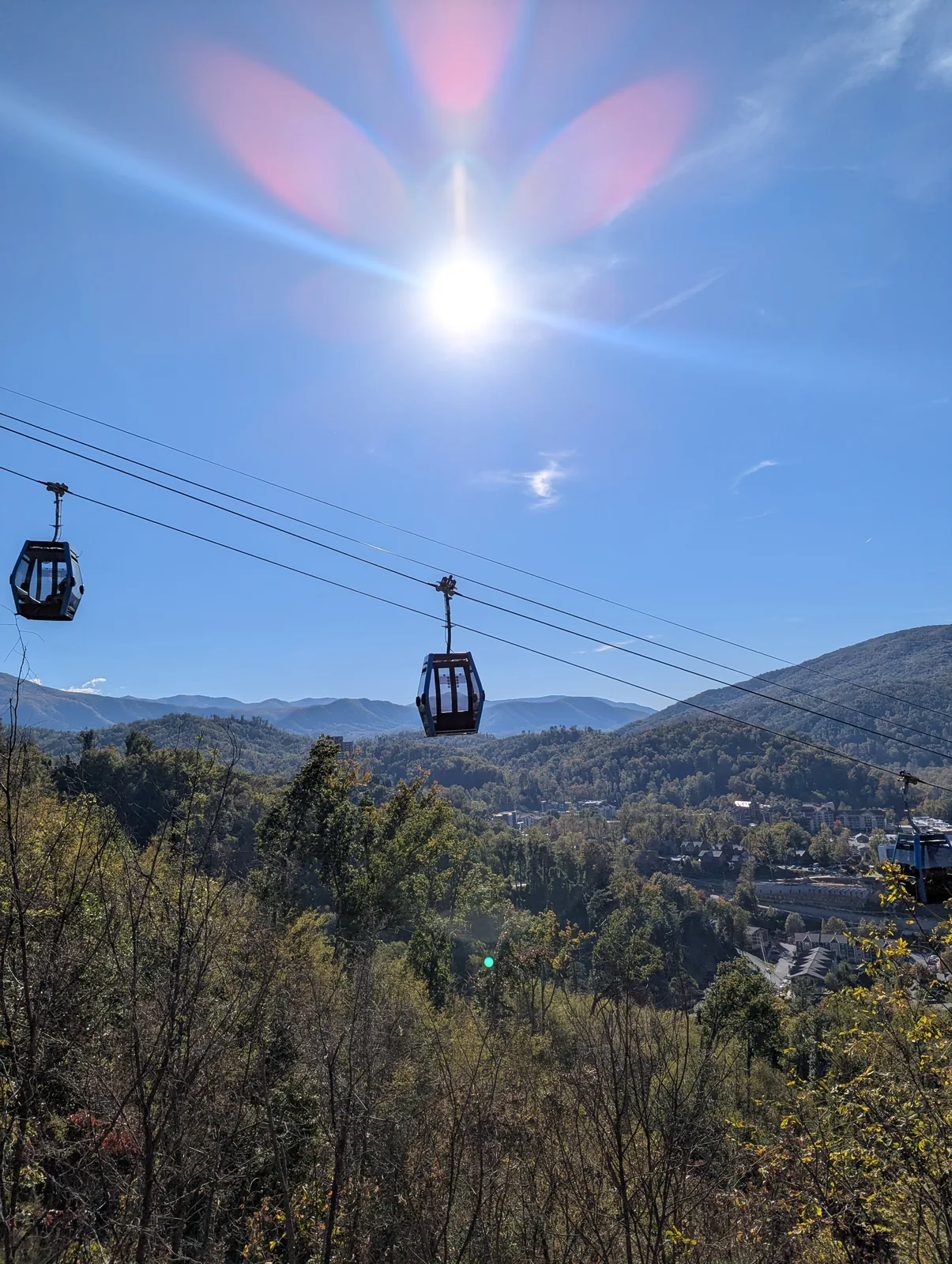 An enclosed gondola cabin seen from another cabin, with a forested valley far below