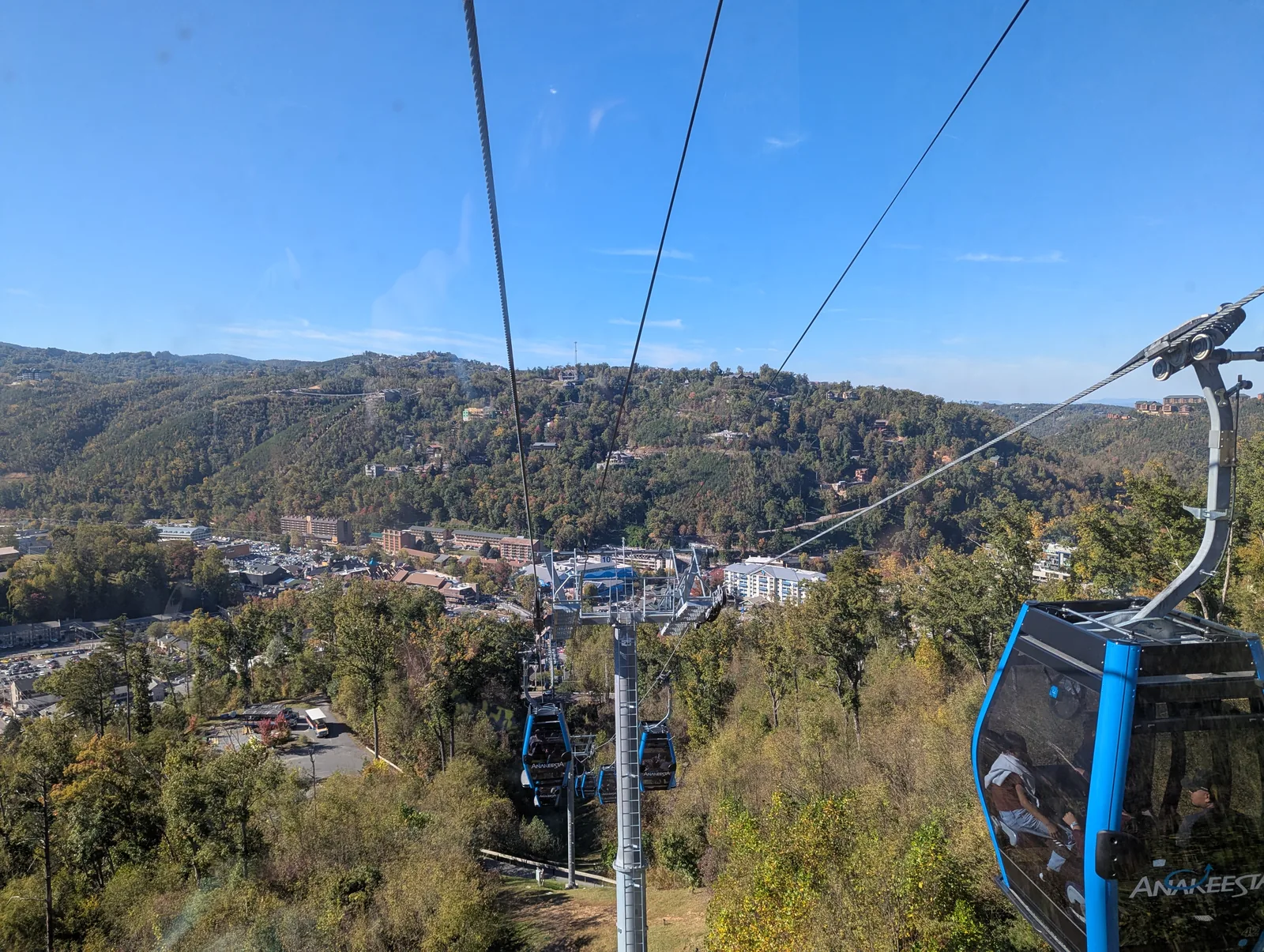 Enclosed blue Anakeesta gondola cabins on the cable line above the town of Gatlinburg, with forested hills behind