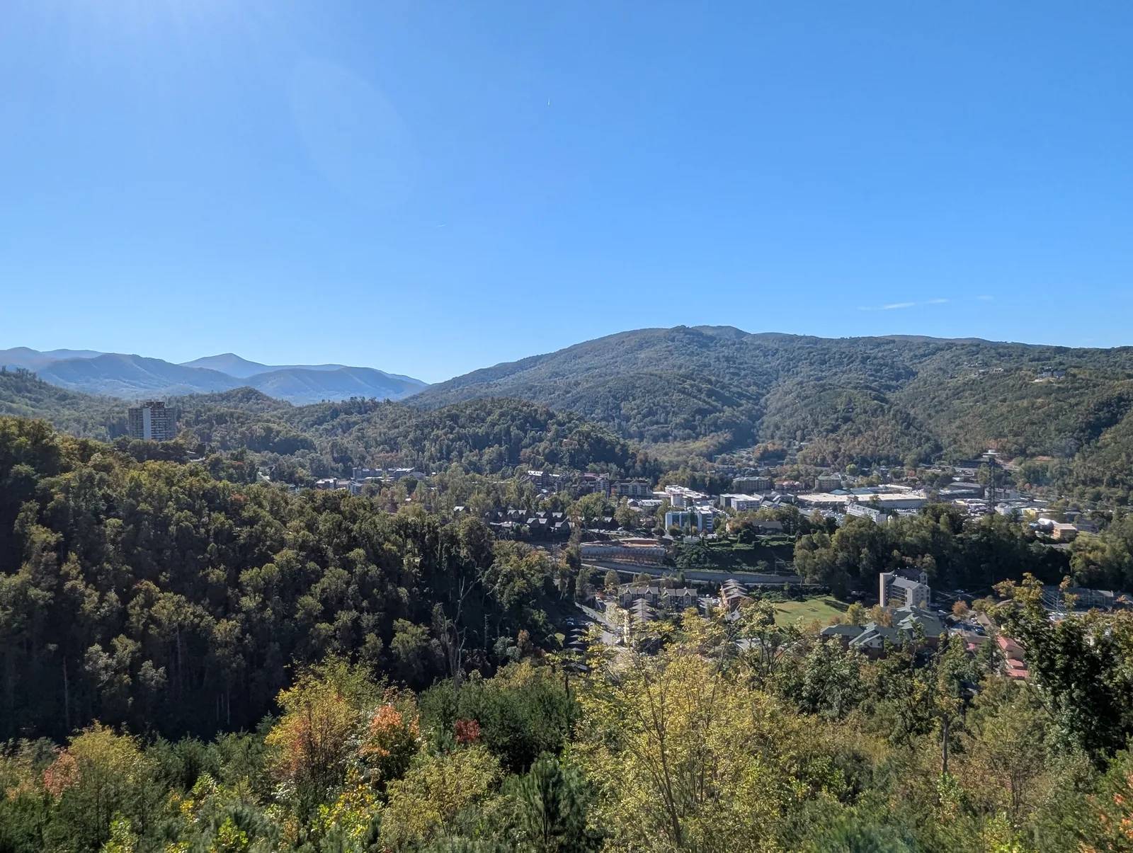 A wide view of layered mountain ridges under a blue sky, with fall color on the near slope