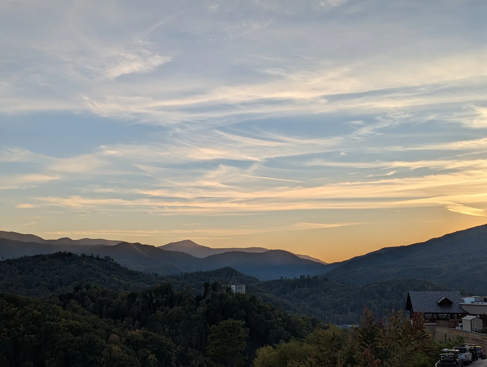 The sun in the left of the frame over a dark mountain ridge, with a pale sky above