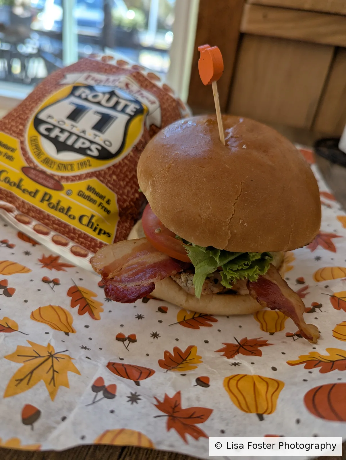 The Rooster, a grilled chicken sandwich on a bun with lettuce, beside a bag of Route 11 kettle chips.