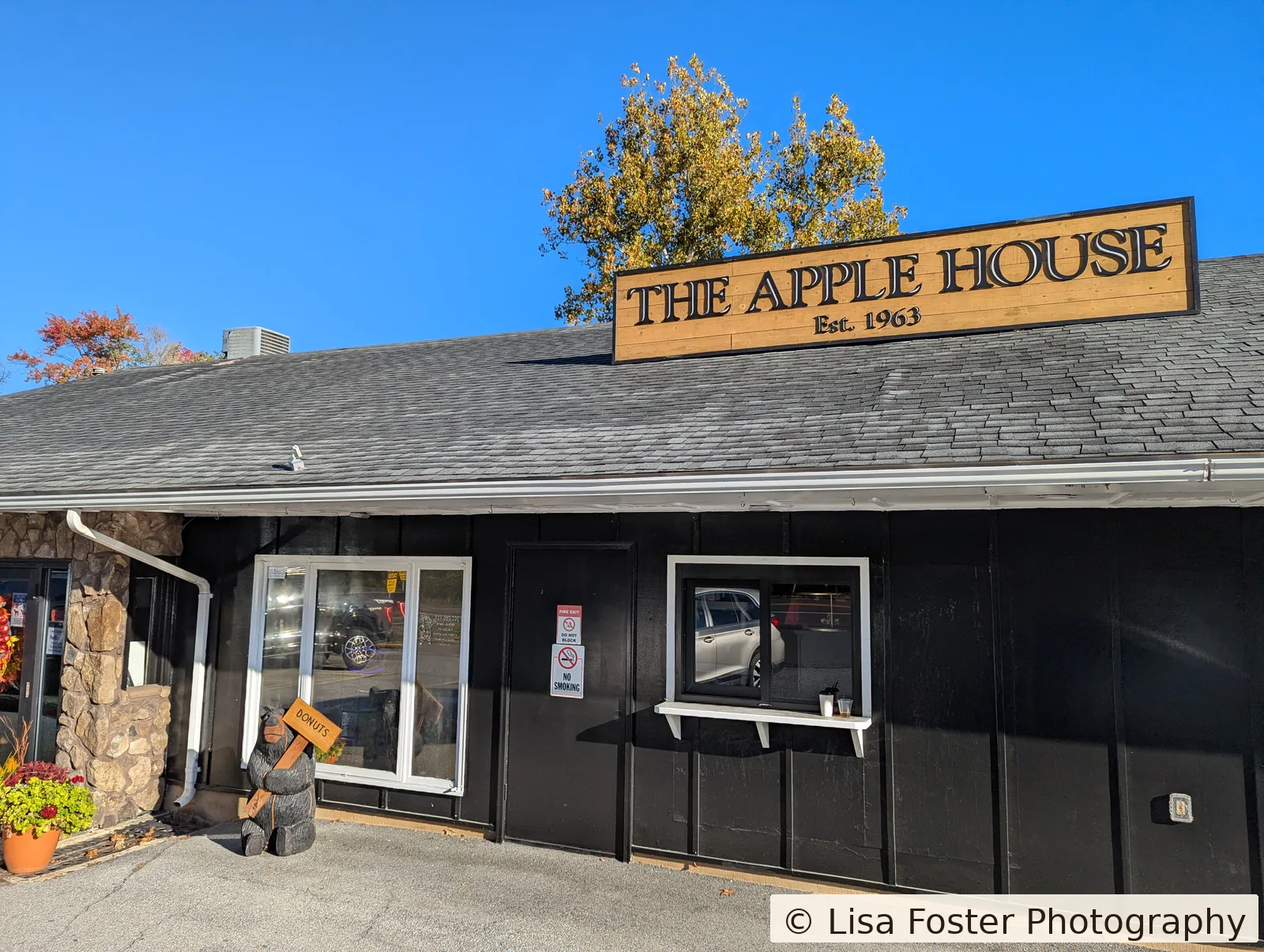 The black board-and-batten Apple House storefront in Linden, with a stone corner, a wood Est. 1963 sign, yellow and orange trees, and a carved bear out front.