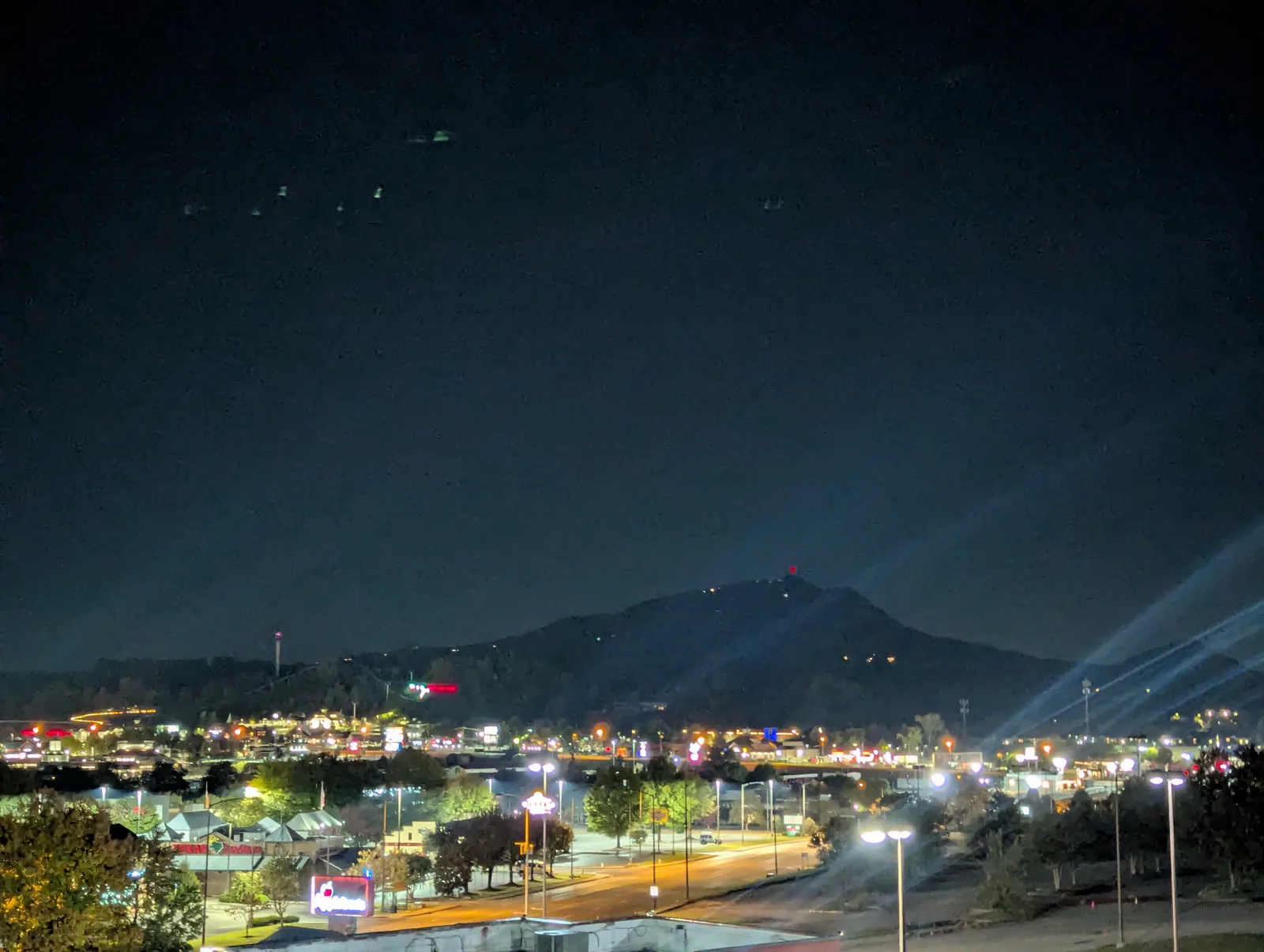 Night view from a balcony over city lights, with the dark outline of a mountain against the sky
