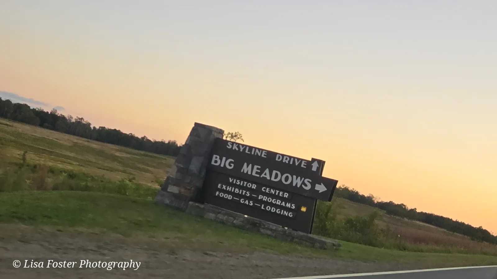 The Big Meadows sign beside Skyline Drive at sunset, seen from a car, with a peach sky over the meadow