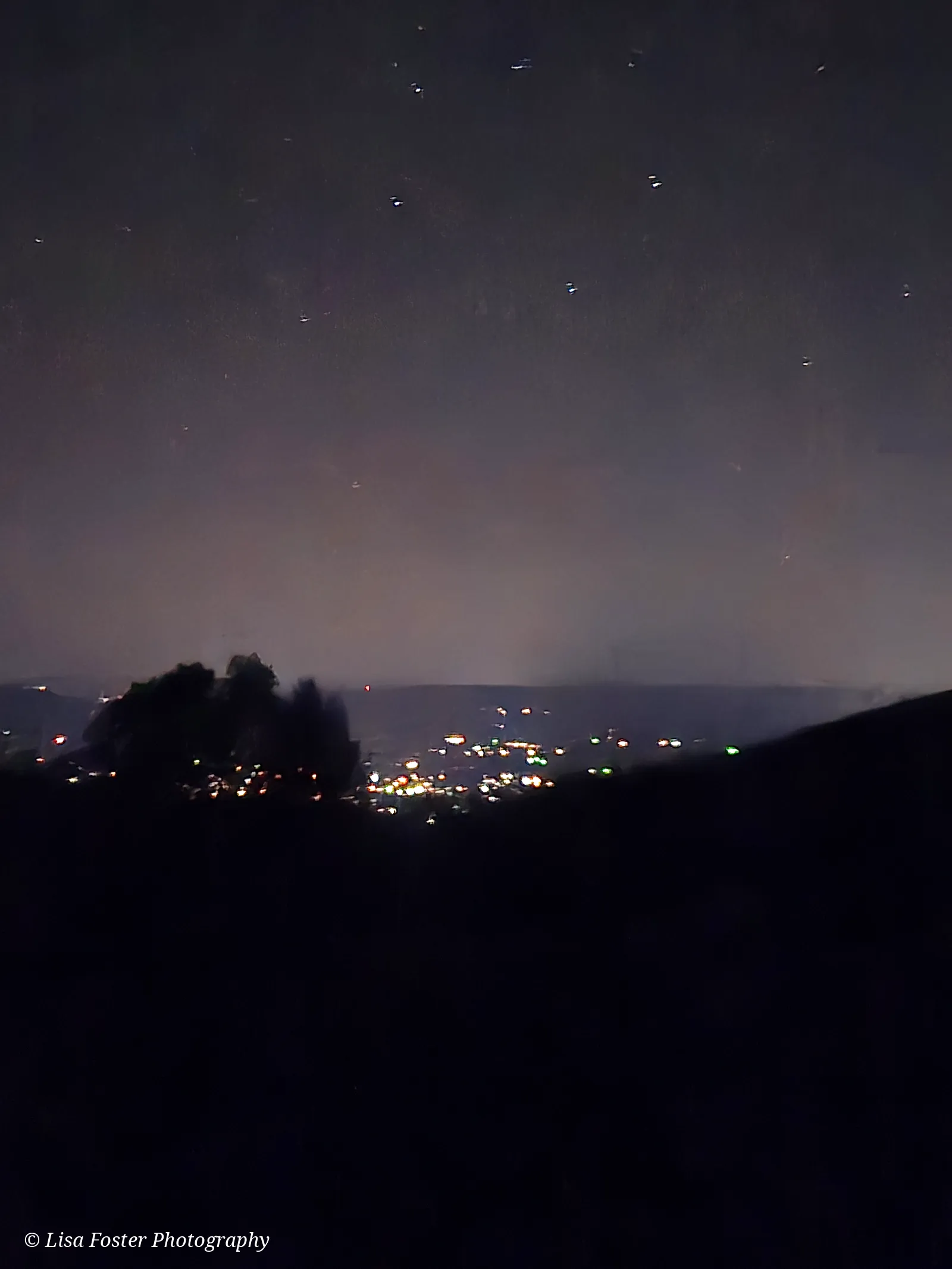 Stars over a dark ridge with town lights glowing in the valley below