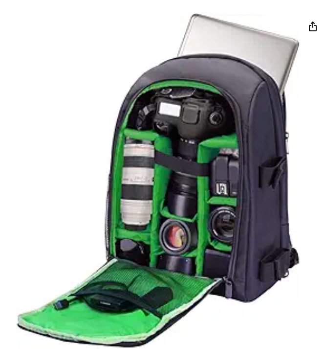 Camera backpack with open flap reveals camera, lenses, and accessories inside green compartments. A laptop peeks from behind the bag.
