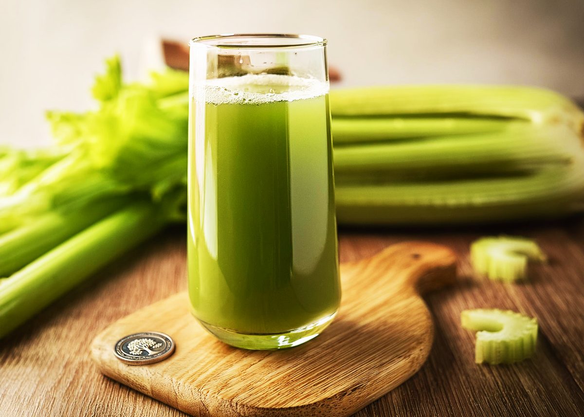 A refreshing glass of celery juice sits on a wooden board, accompanied by fresh celery stalks, highlighting its natural and healthy appeal.