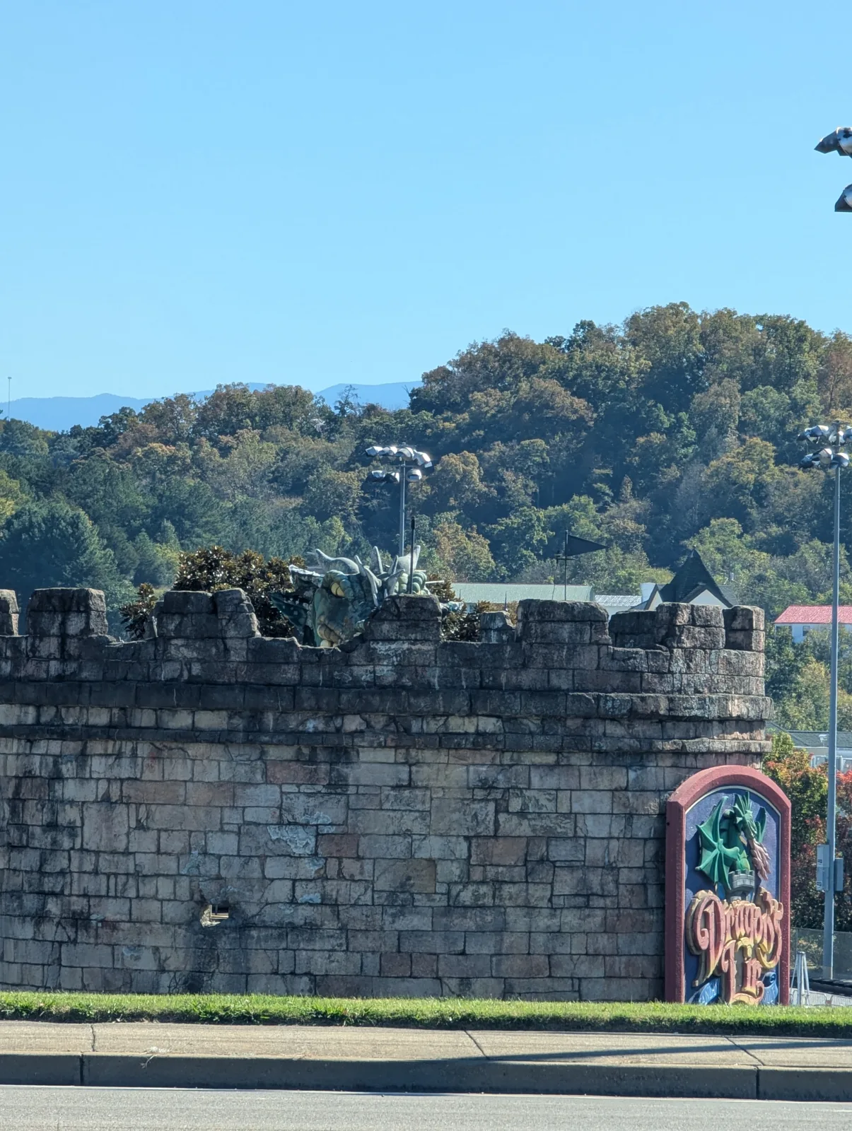 A stone castle wall with a green dragon peeking over the top and a "Dragon's Lair" sign, wooded hills behind