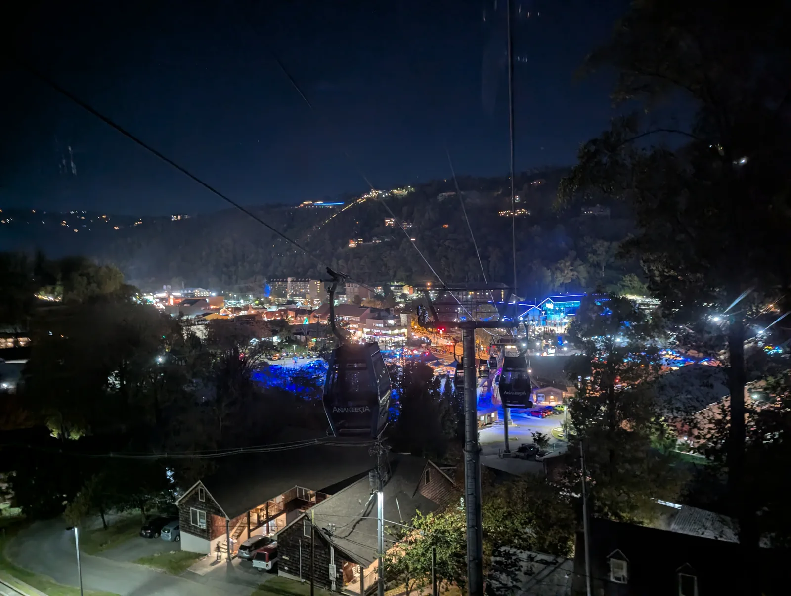 A gondola cable and an enclosed cabin in the foreground, with town lights filling the valley at night
