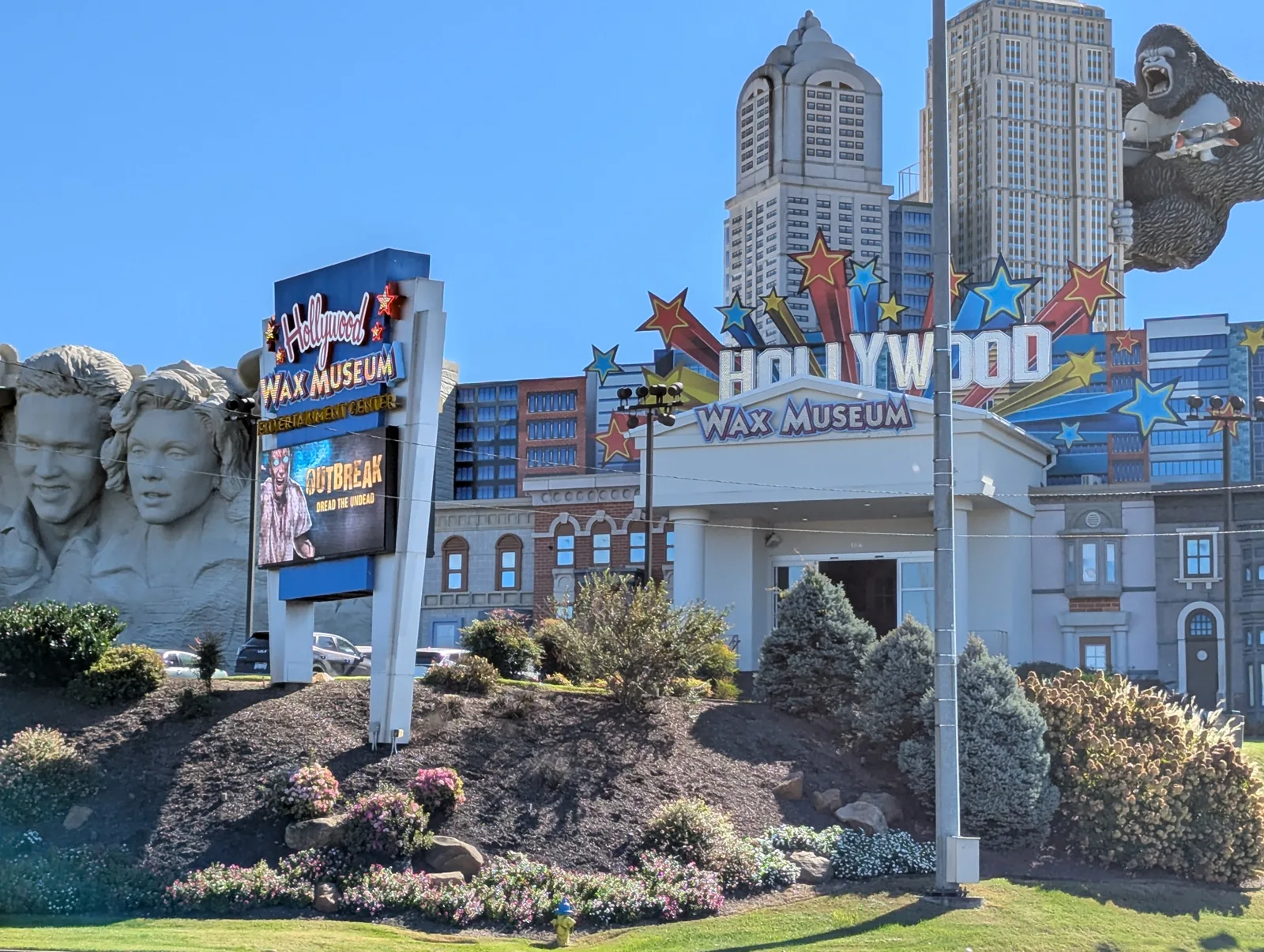 The Hollywood Wax Museum entrance with a "Hollywood" star sign, large stone celebrity faces carved into a rock wall, and a replica skyline with King Kong on a tower