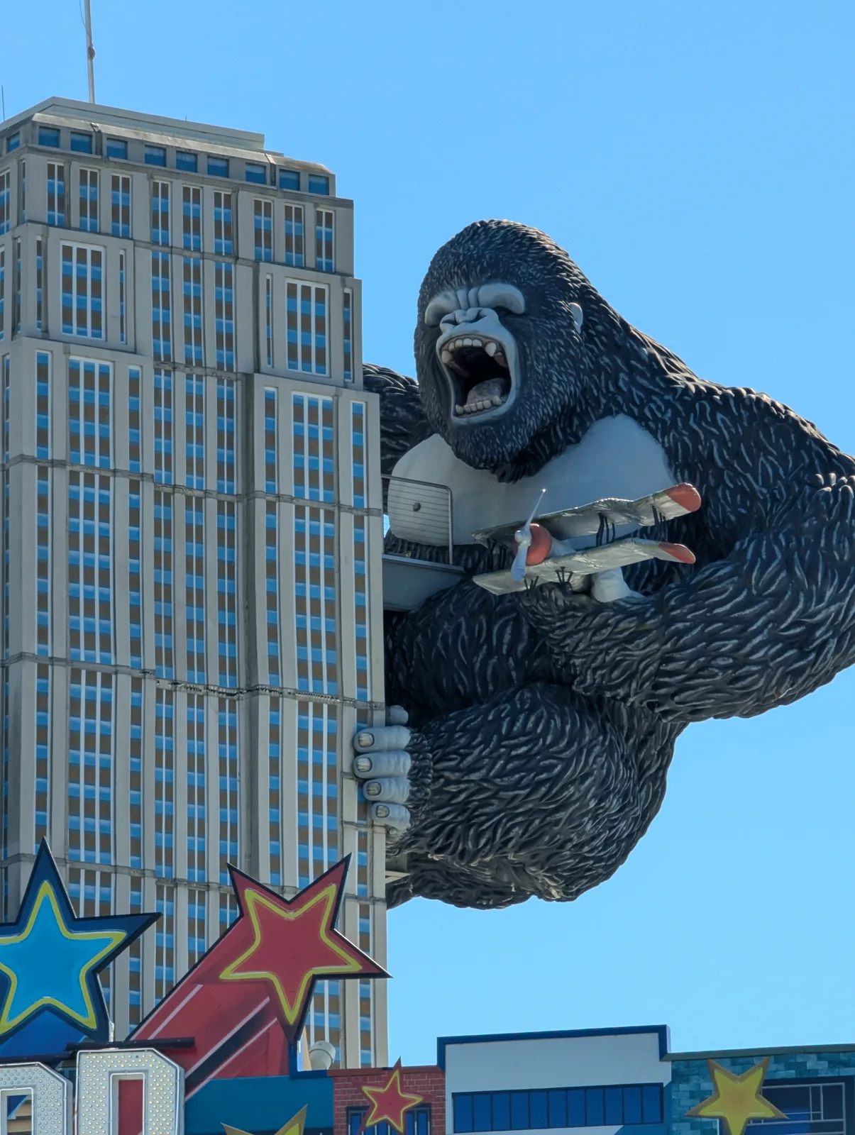 A large King Kong figure gripping the side of a tall replica skyscraper against a blue sky