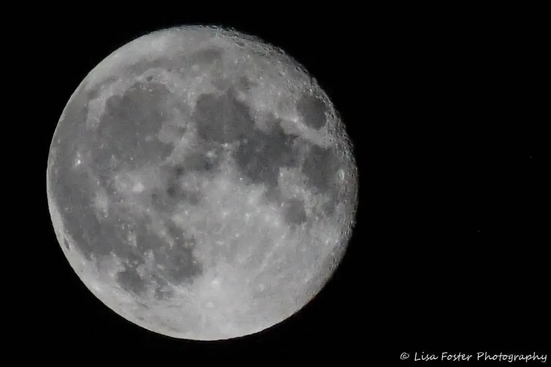 A bright full Moon in sharp detail against a black sky, with its craters and dark seas clearly visible