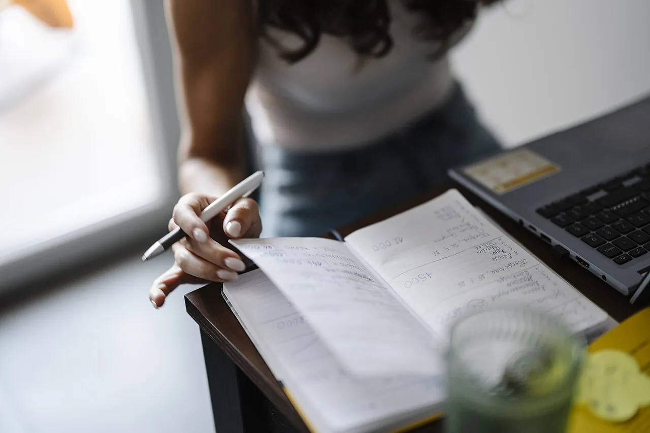 A person writing in a paper notebook at a desk