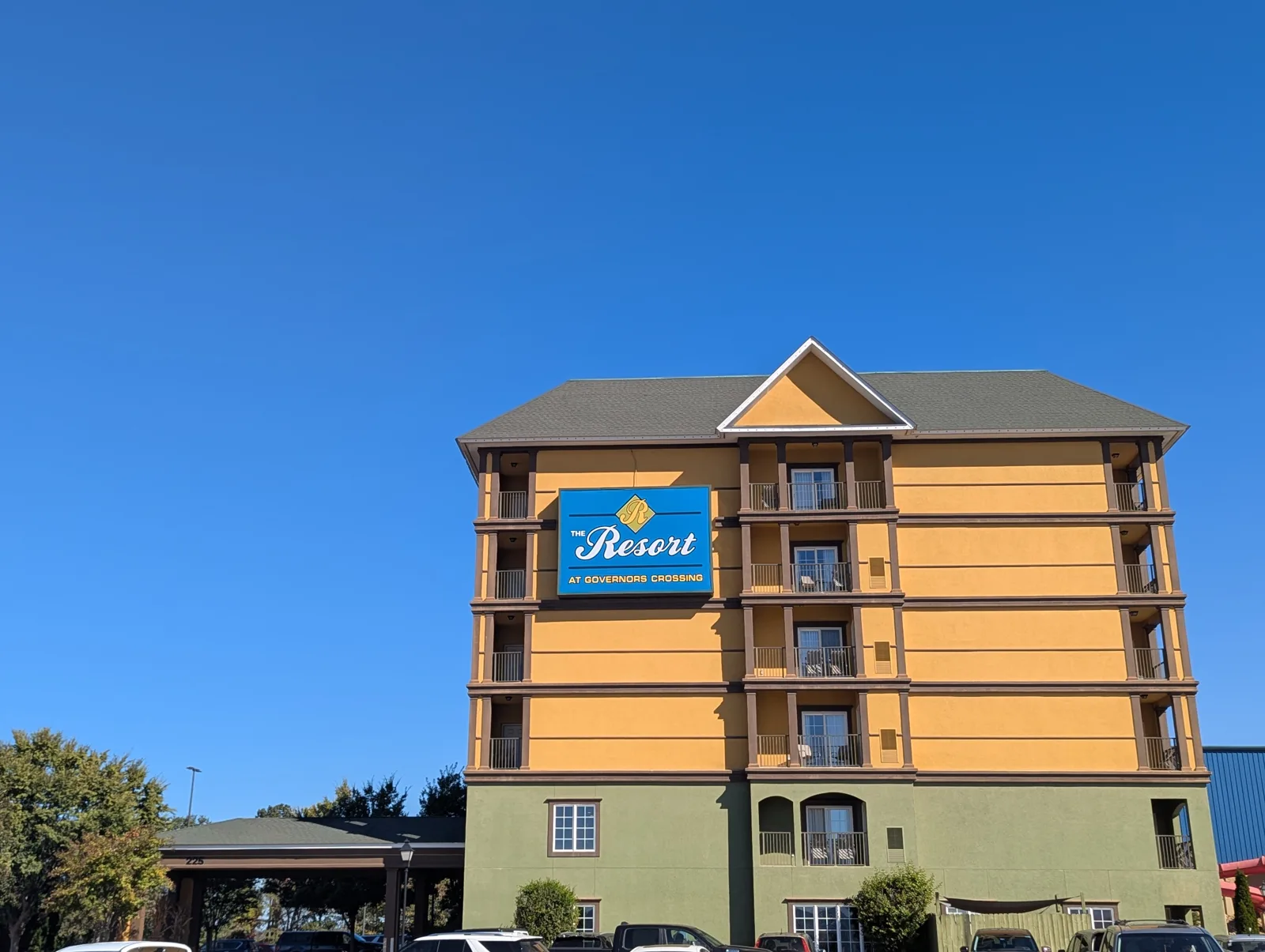 The Resort at Governor's Crossing, a mustard-yellow and green six-story building with a blue "The Resort" sign, under a clear blue sky