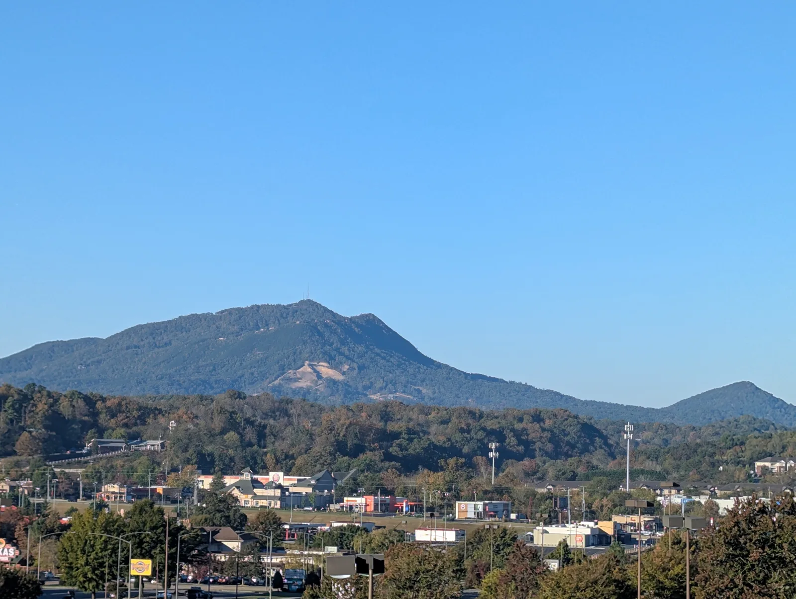 View over rooftops and shops toward a forested mountain under a clear morning sky