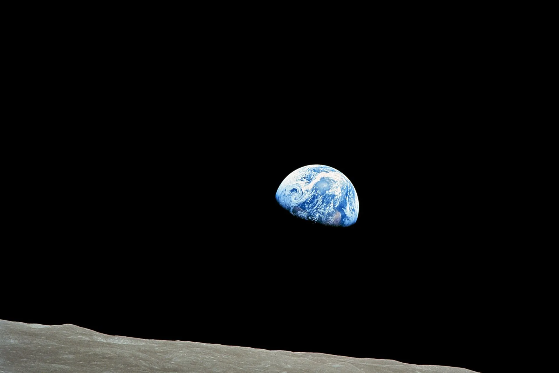 Earth rising over the gray, cratered horizon of the Moon, photographed from Apollo 8